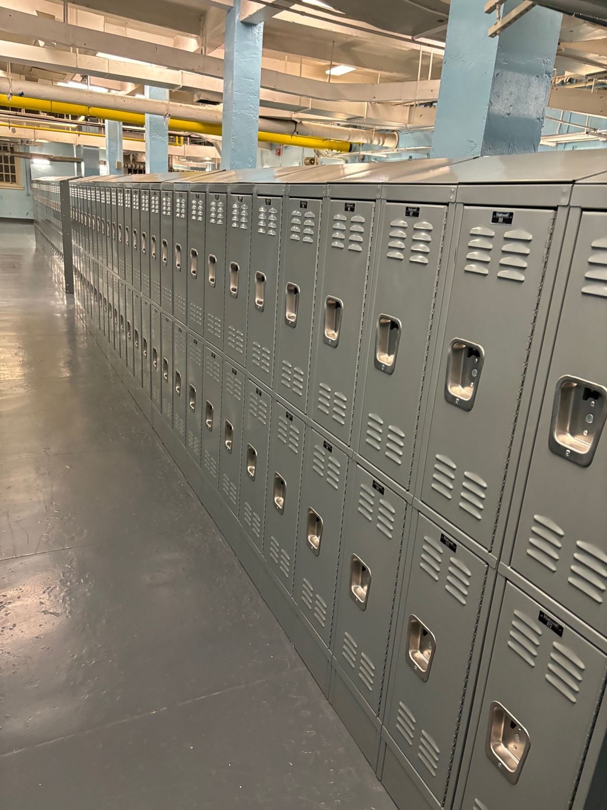 Long run of new grey steel lockers on a freshly coated floor at Jamaica High School in Queens