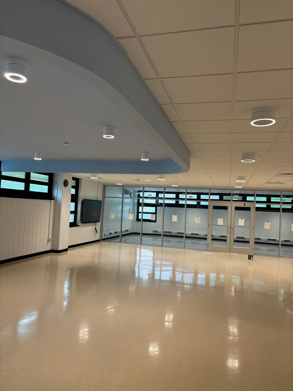 Renovated multipurpose room with a curved blue ceiling soffit, ring lights and a glazed partition wall